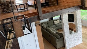 A loft-style room with a wooden ceiling, a loft bed, a sofa, and a stone fireplace.