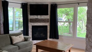A living room with a fireplace, a sofa, a coffee table, and large windows.
