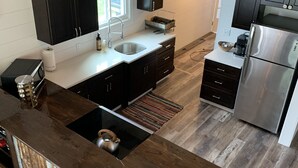 A modern kitchen with a central island, dark cabinetry, stainless steel appliances, and a rustic wooden floor.