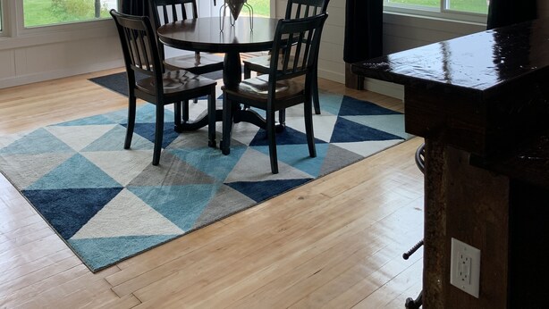 A dining area with a wooden table and chairs, a clock on the wall, and large windows offering a view of the outdoors.