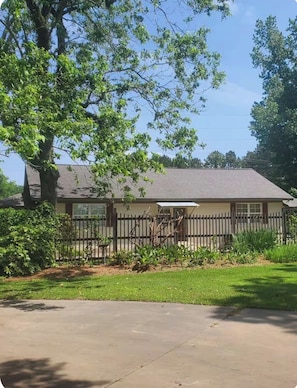 A single-story house with a fenced yard, a large tree, and a clear sky.