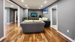 A modern living room with hardwood flooring, a grey sofa, a flat-screen TV, and a painting on the wall. - CHeerful 3-bedroom waterfront home (Riviera Beach)