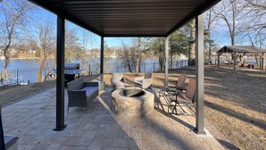 An outdoor patio with stone flooring, wicker furniture, a fire pit, and a view of a lake and dock. - CHeerful 3-bedroom waterfront home (Riviera Beach)