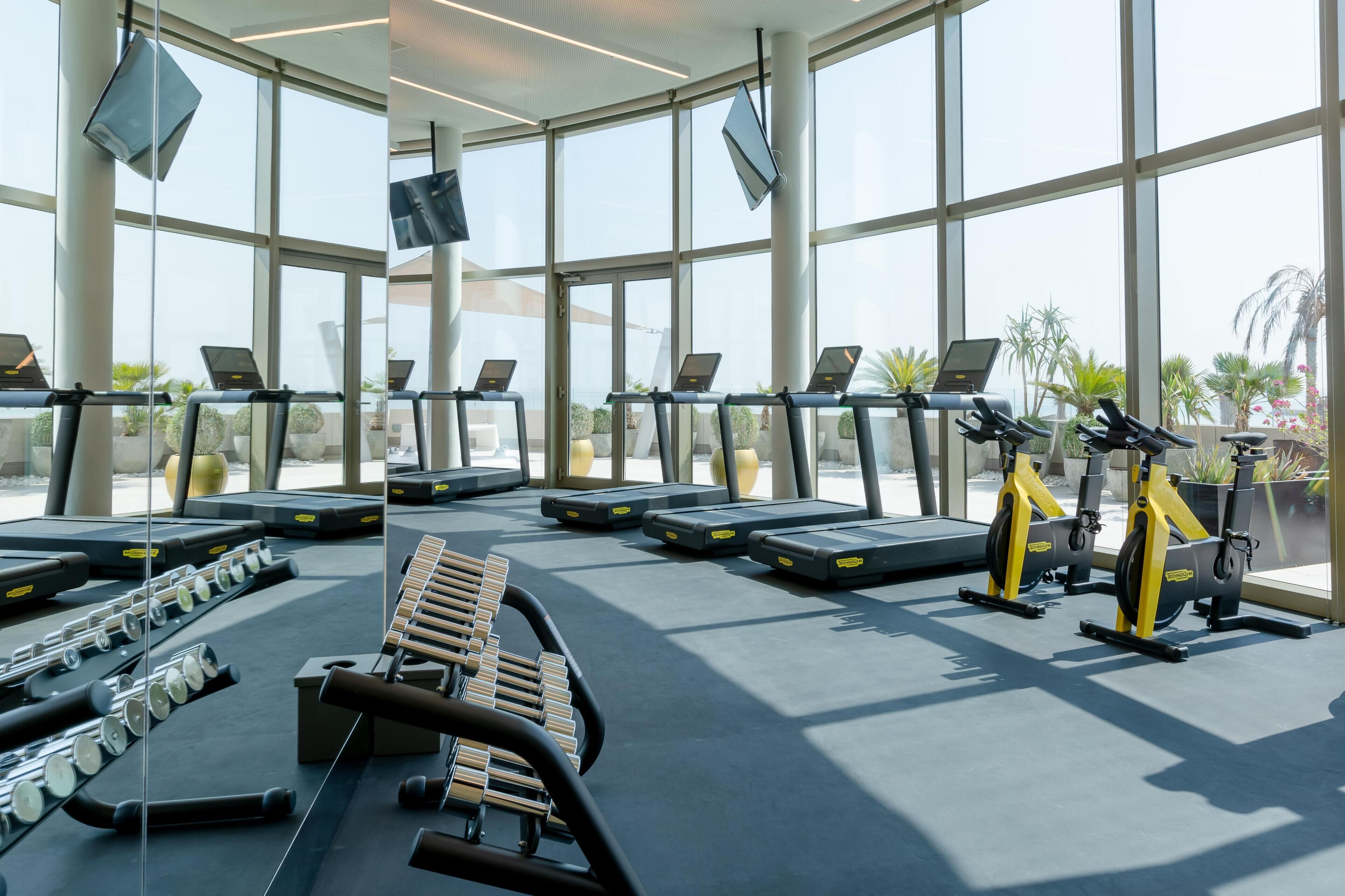 Une salle de sport équipée de tapis de course, de vélos d’appartement et d’haltères.