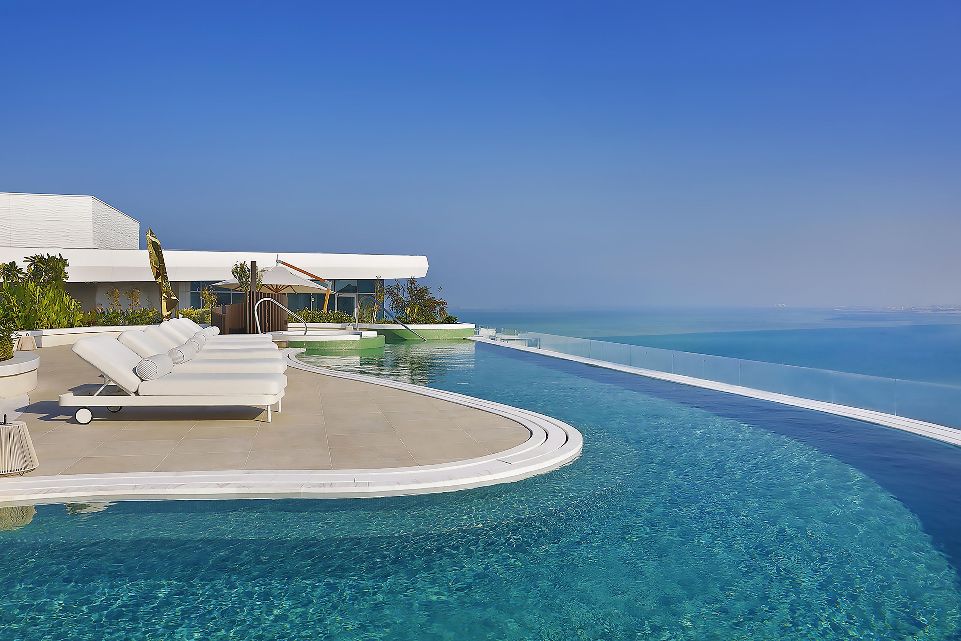 Une piscine à débordement avec une eau d’un bleu cristallin, des chaises longues blanches et une vue sur l’océan.