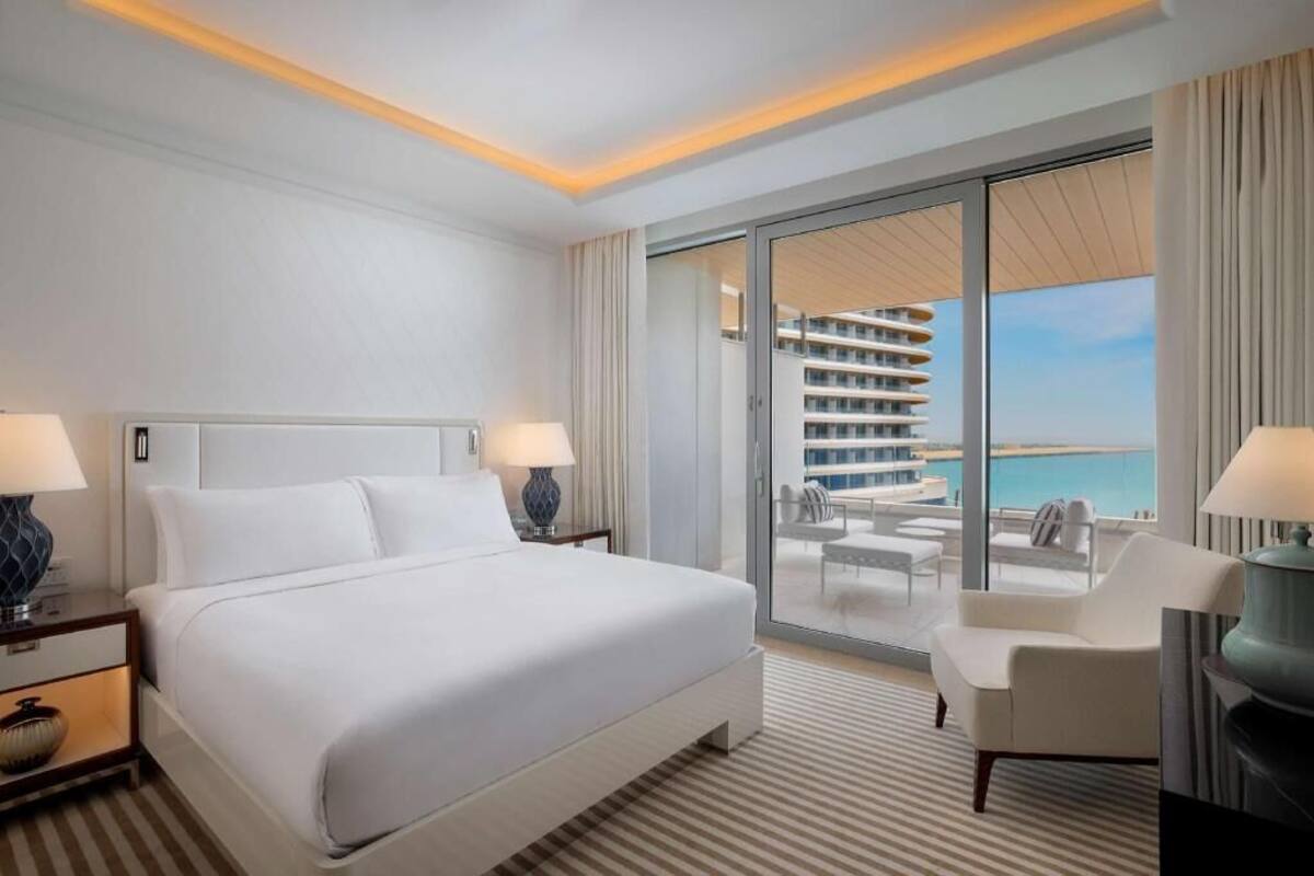 A hotel room with a large bed, a balcony with a view of the sea, and a seating area with a table and chairs.