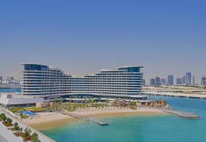 A modern hotel with a curved facade, a beach, and a water body in the foreground. - Waldorf Astoria Doha Lusail (Lusail)
