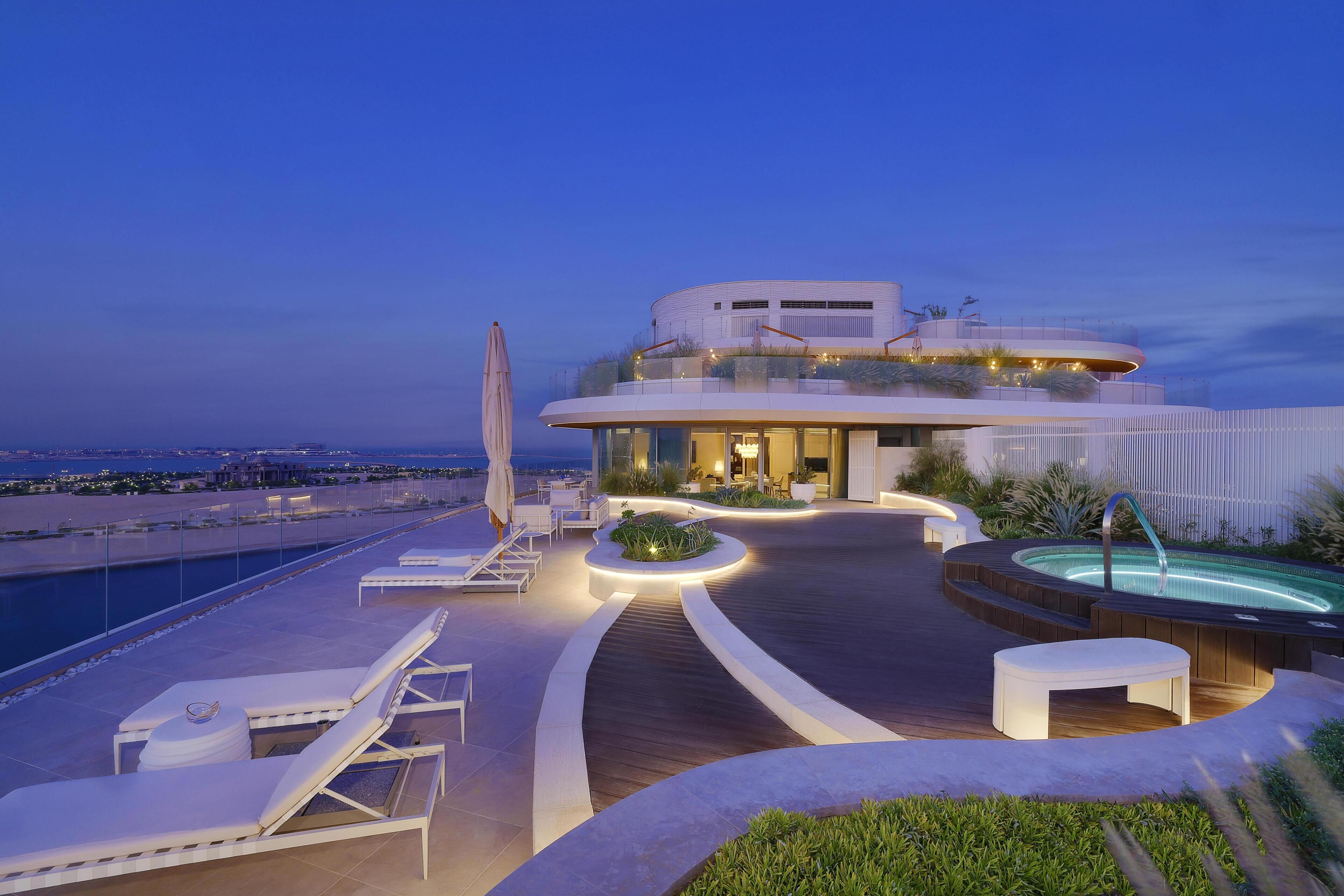 A modern building with a pool, lounge chairs, and a view of the ocean.