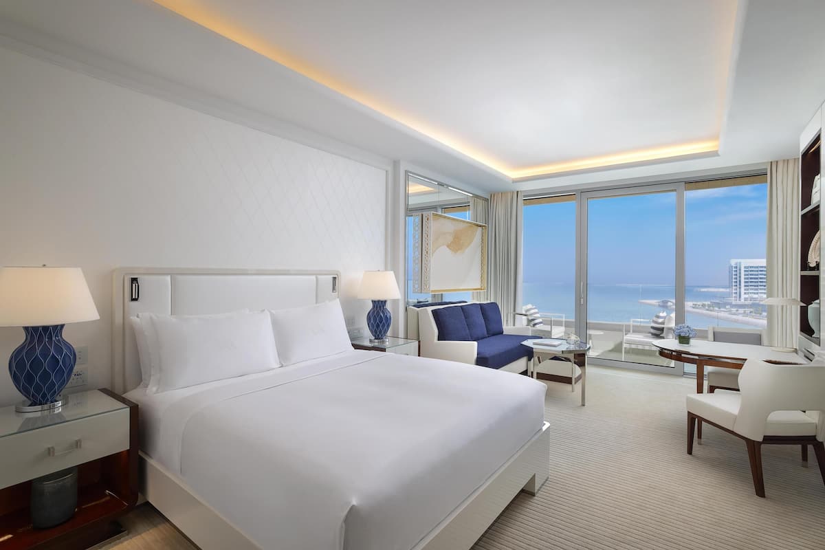 A hotel room with a large bed, a sofa, a desk, and a view of the city.