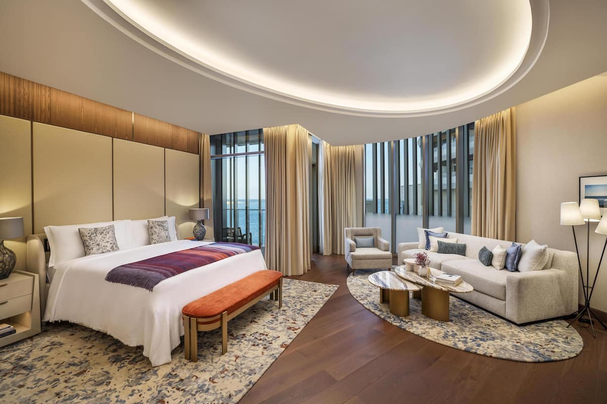 A modern hotel room with a large bed, a sofa, a coffee table, and a view of the city.