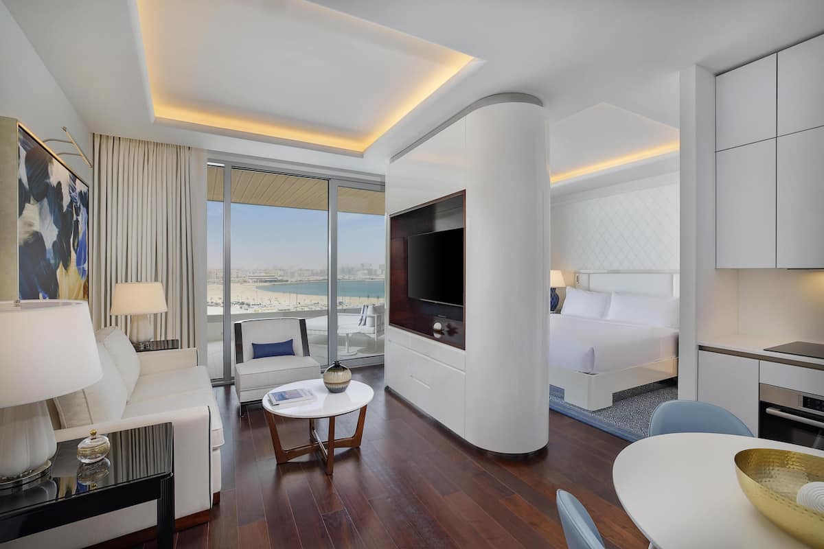 A modern hotel room with a large TV, a sofa, a dining table, and a bed.