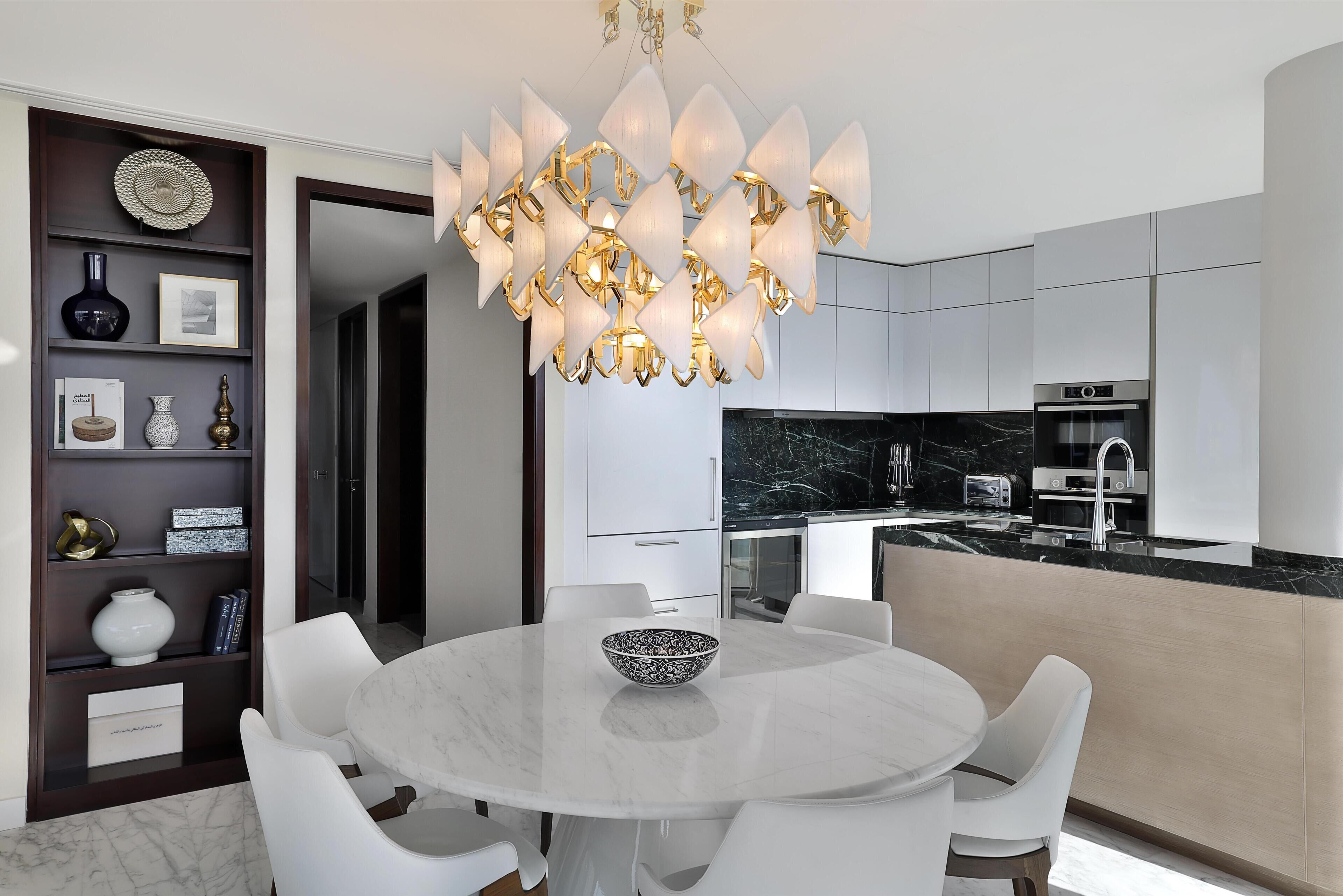 A modern kitchen with a marble countertop, built-in appliances, and a unique chandelier.