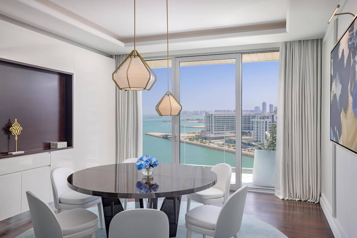 A modern dining area with a round table, white chairs, and a city view through large windows.