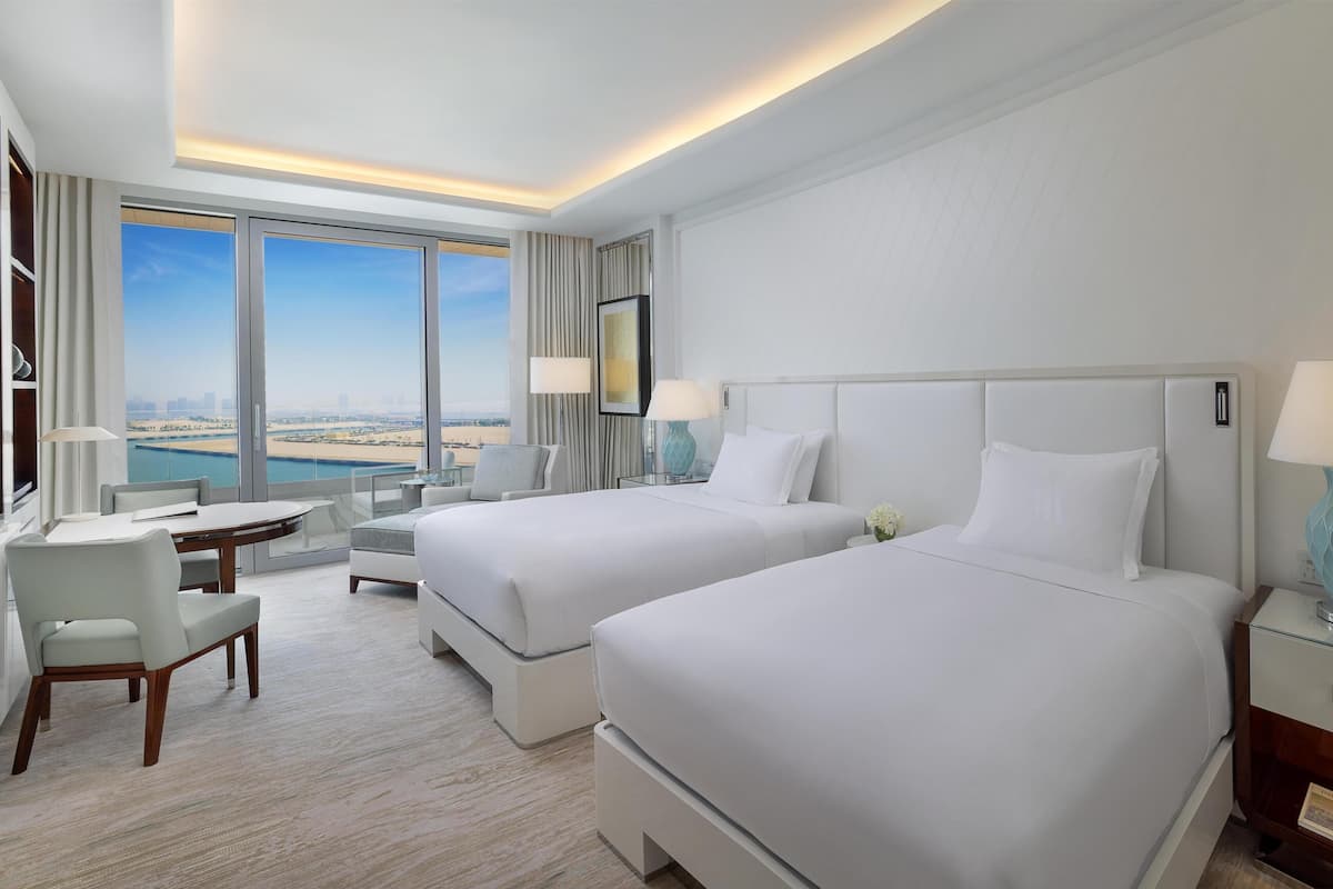 A hotel room with two beds, a desk, a chair, and a large window with a view.