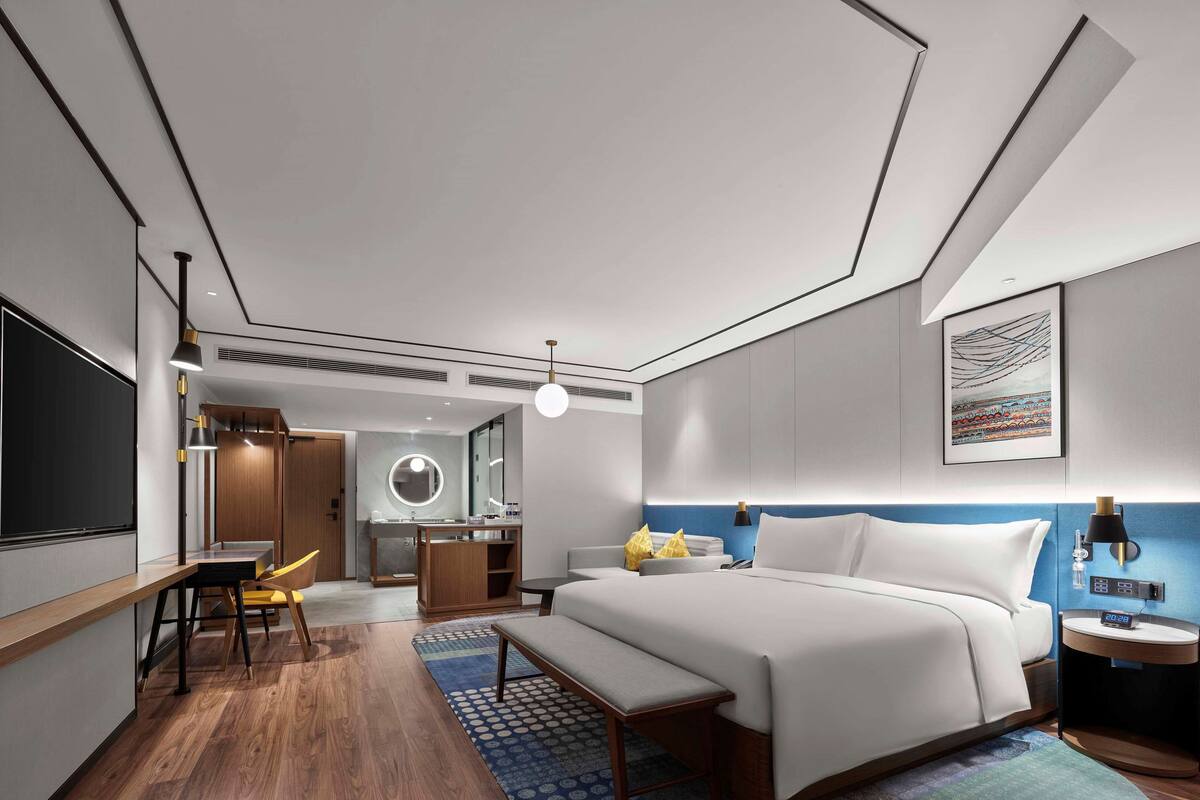 A modern hotel room with a large bed, a desk, a vanity, and a bathroom.