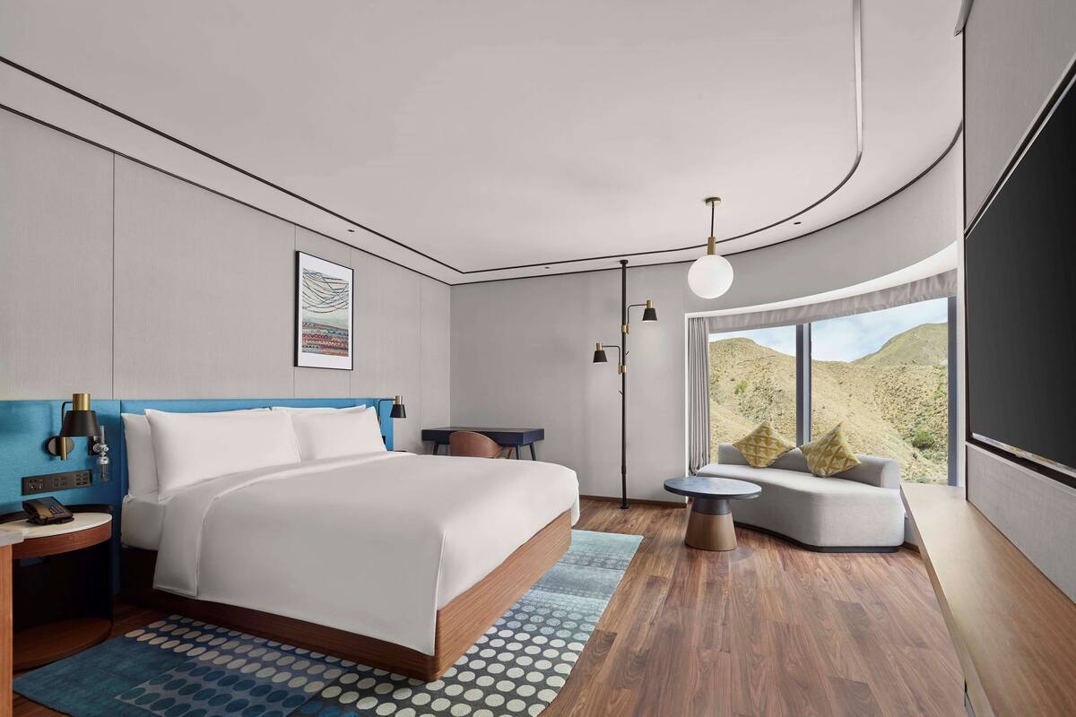 A modern hotel room with a large bed, a desk, a seating area, and a view of a desert landscape.