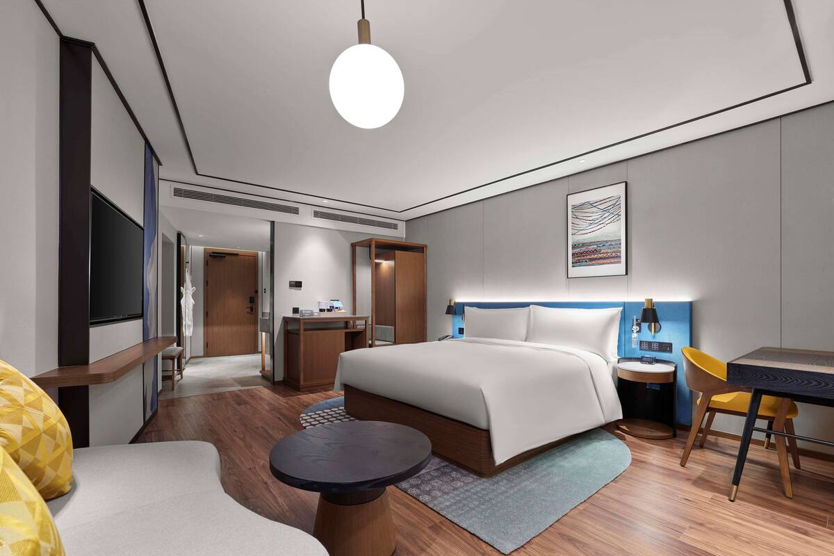 A modern hotel room with a large bed, a desk, a chair, and a television.