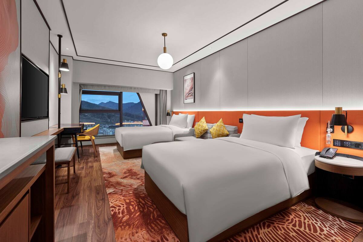 A hotel room with two beds, a desk, and a view of mountains.