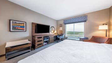 A hotel room with a large bed, a flat-screen TV, a desk with a chair, a window with a view, and a wall-mounted TV.