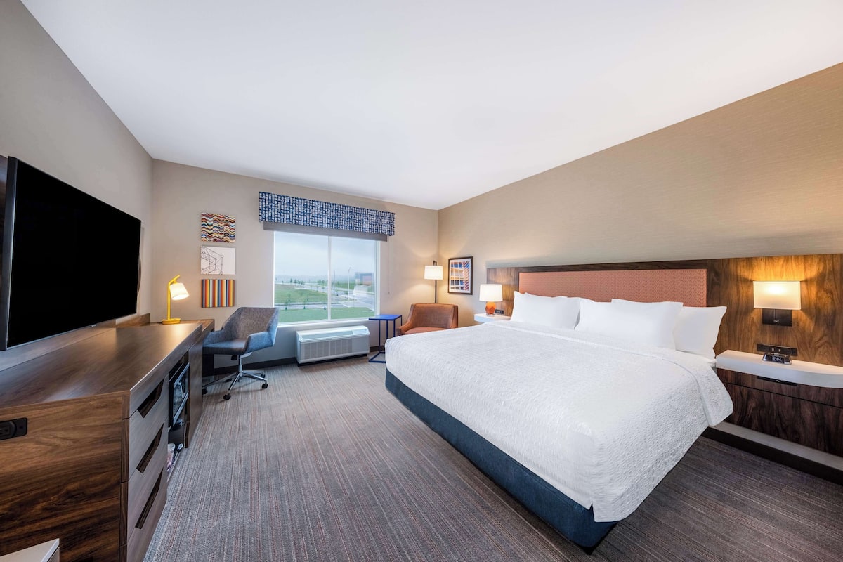 Una habitación de hotel con una cama grande, un escritorio con un televisor de pantalla plana, una silla y una ventana con vista a la ciudad.