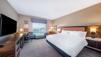 Une chambre d’hôtel avec un grand lit, un bureau doté d’une télévision à écran plat, une chaise et une fenêtre donnant sur la ville.