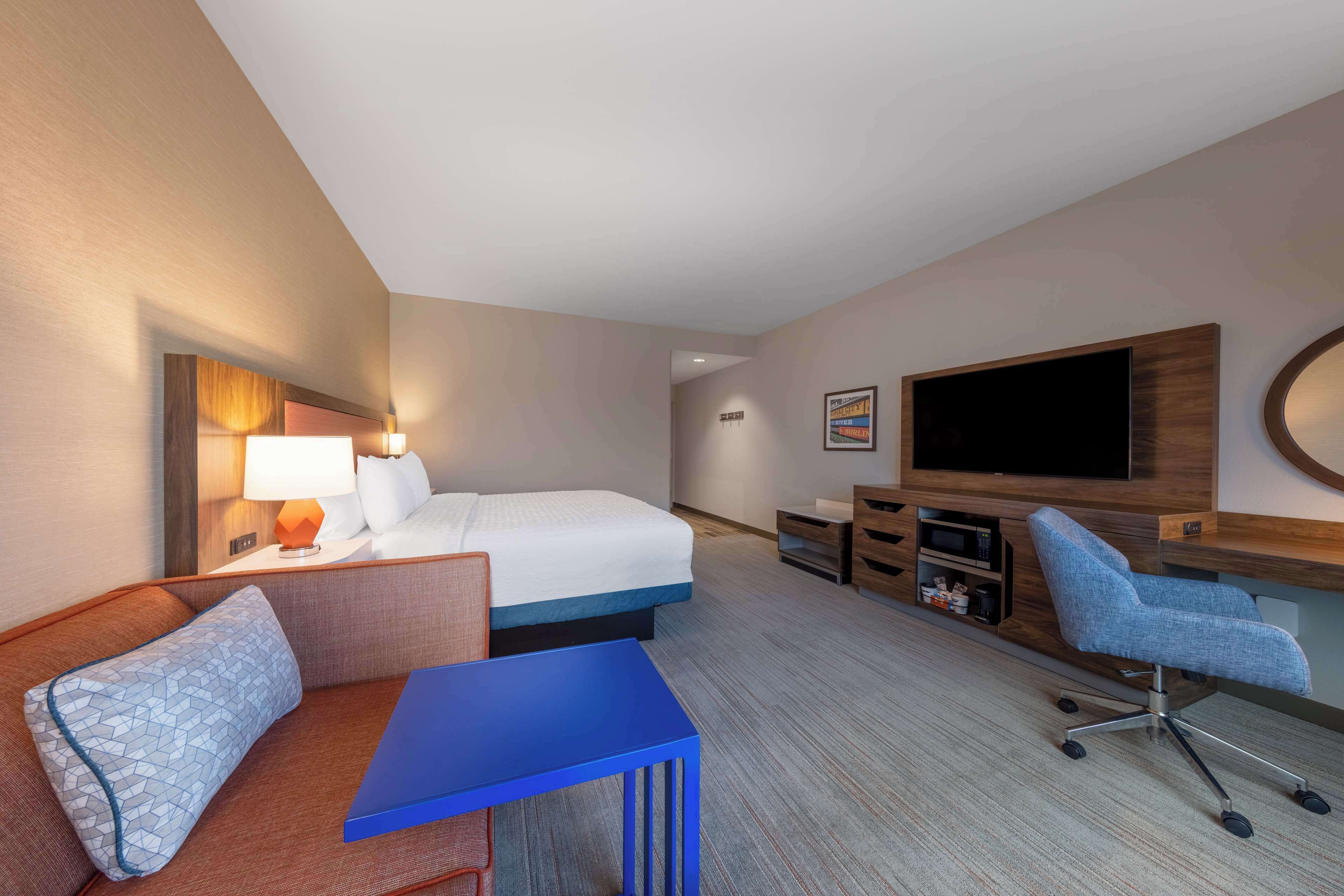 A hotel room with a bed, a desk, a chair, a TV, and a small table.