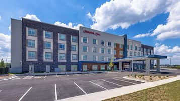 A Hampton Inn hotel with a parking lot, a covered entrance, and a clear blue sky.