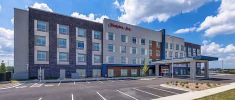 A Hampton Inn hotel with a parking lot, a covered entrance, and a clear blue sky.