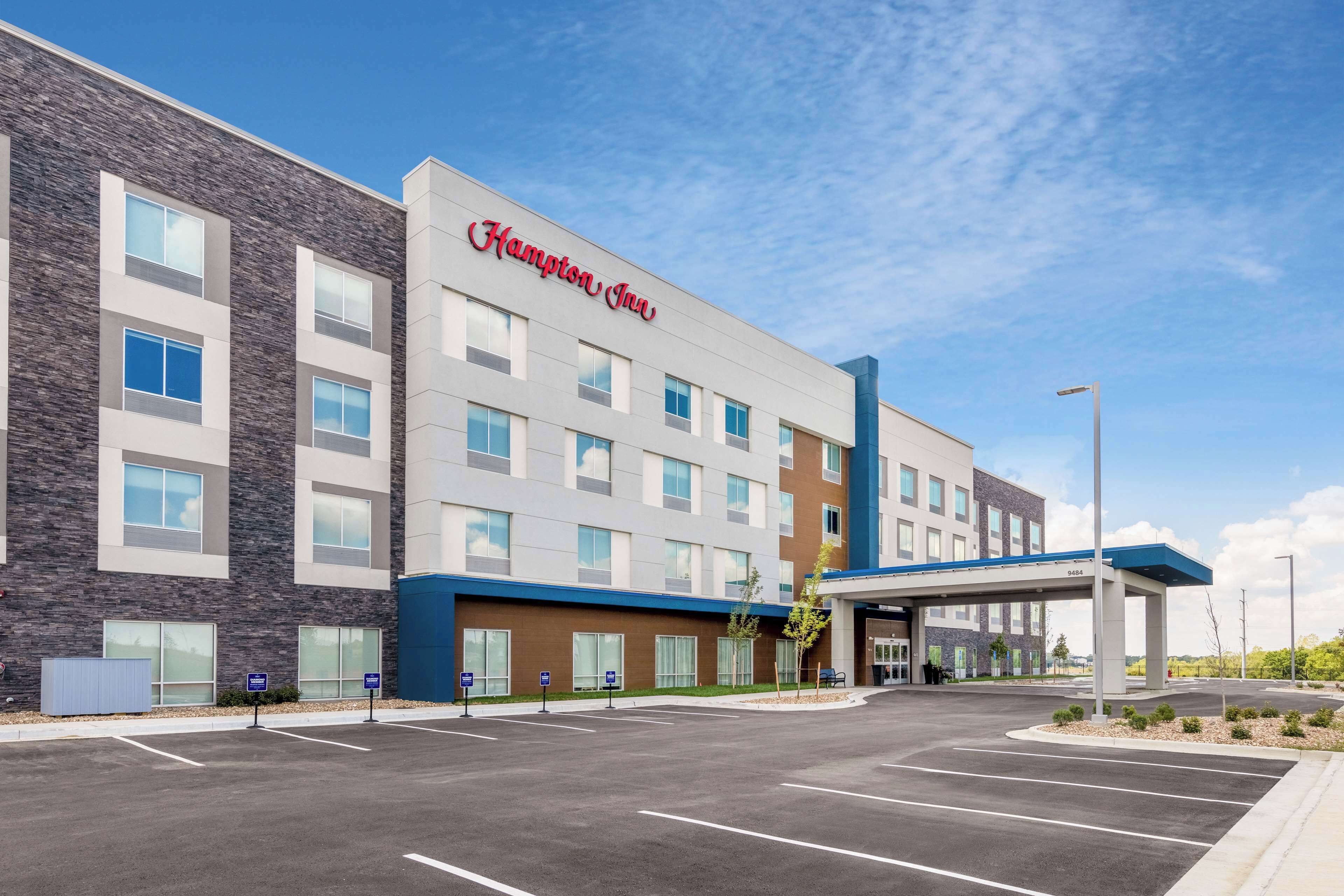 Um hotel Hampton Inn com design moderno, que inclui um amplo estacionamento e entrada coberta.