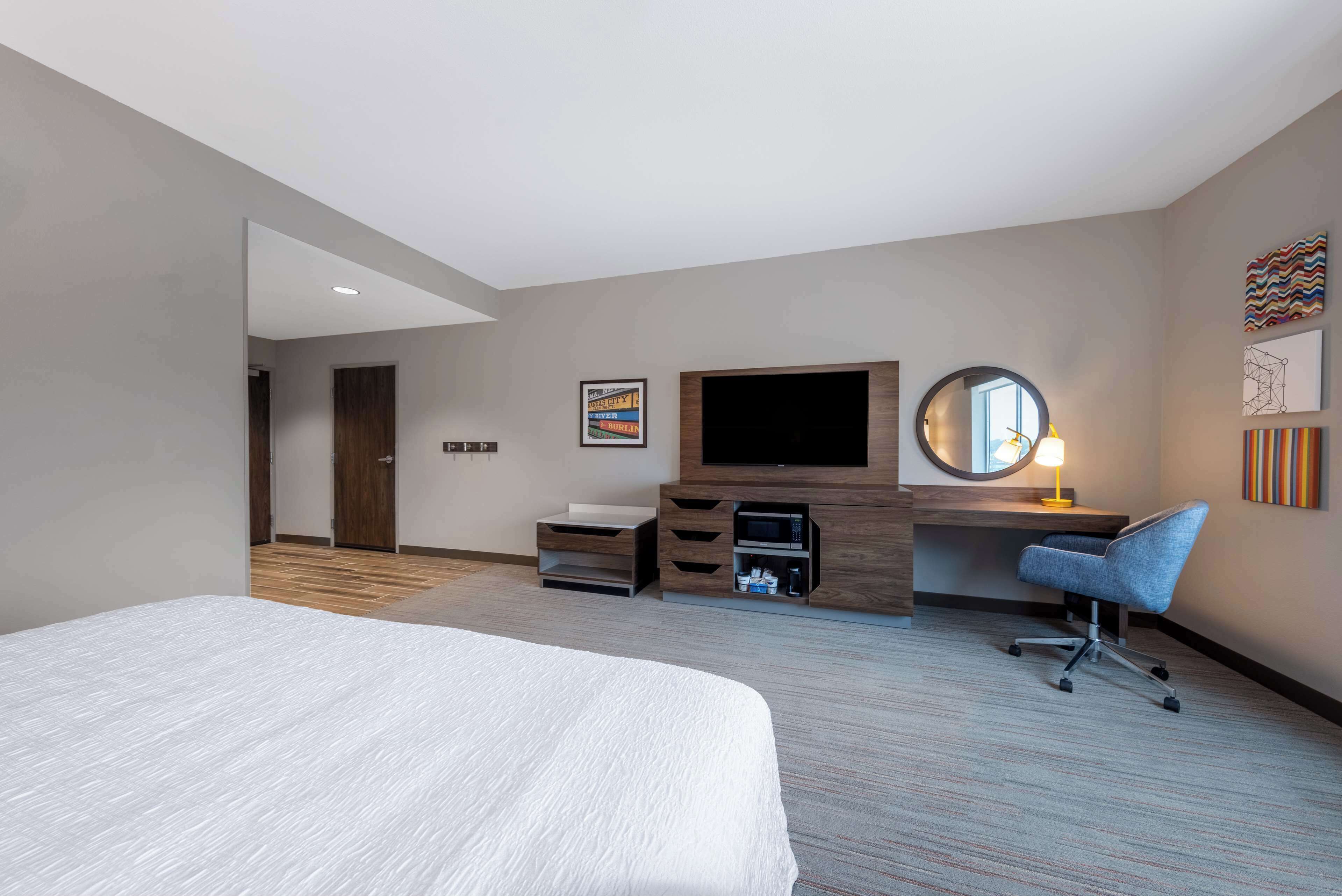 Una habitación de hotel con cama, escritorio con computadora, televisor, espejo y silla.