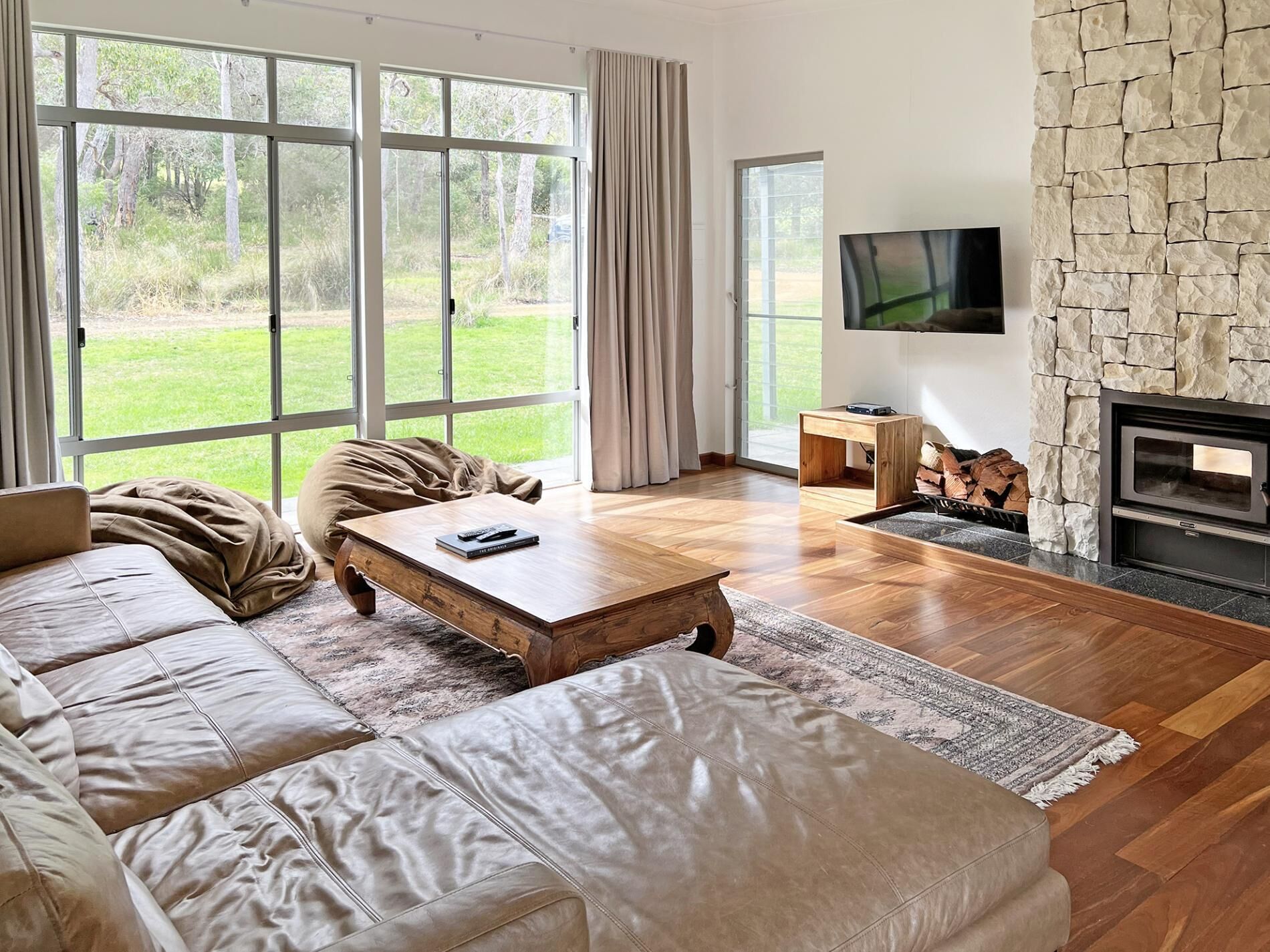 A spacious living room with a large sofa, a wooden coffee table, a stone fireplace, and a television mounted on the wall.