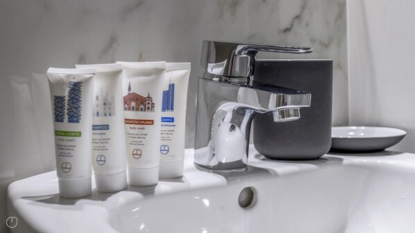 A bathroom sink with toiletries, a modern faucet, and a marble wall. - Italianway - The B Village Standard - T5 (Milan)