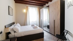 A bedroom with a bed, a nightstand, a lamp, a wardrobe, and a chair. - Italianway Easy - Muratori 8 (Milan)