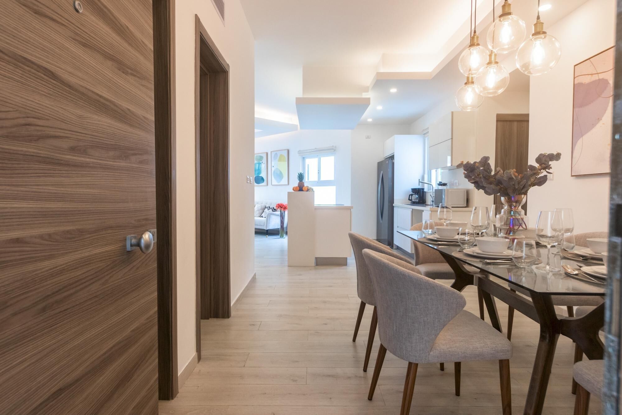 A modern kitchen with a central island, dining table with chairs, and a refrigerator.