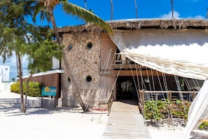 A stone building with a thatched roof and a wooden deck leading to a covered area.