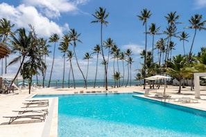 Un espace aménagé au bord de la piscine, avec des chaises longues, une piscine et des palmiers.