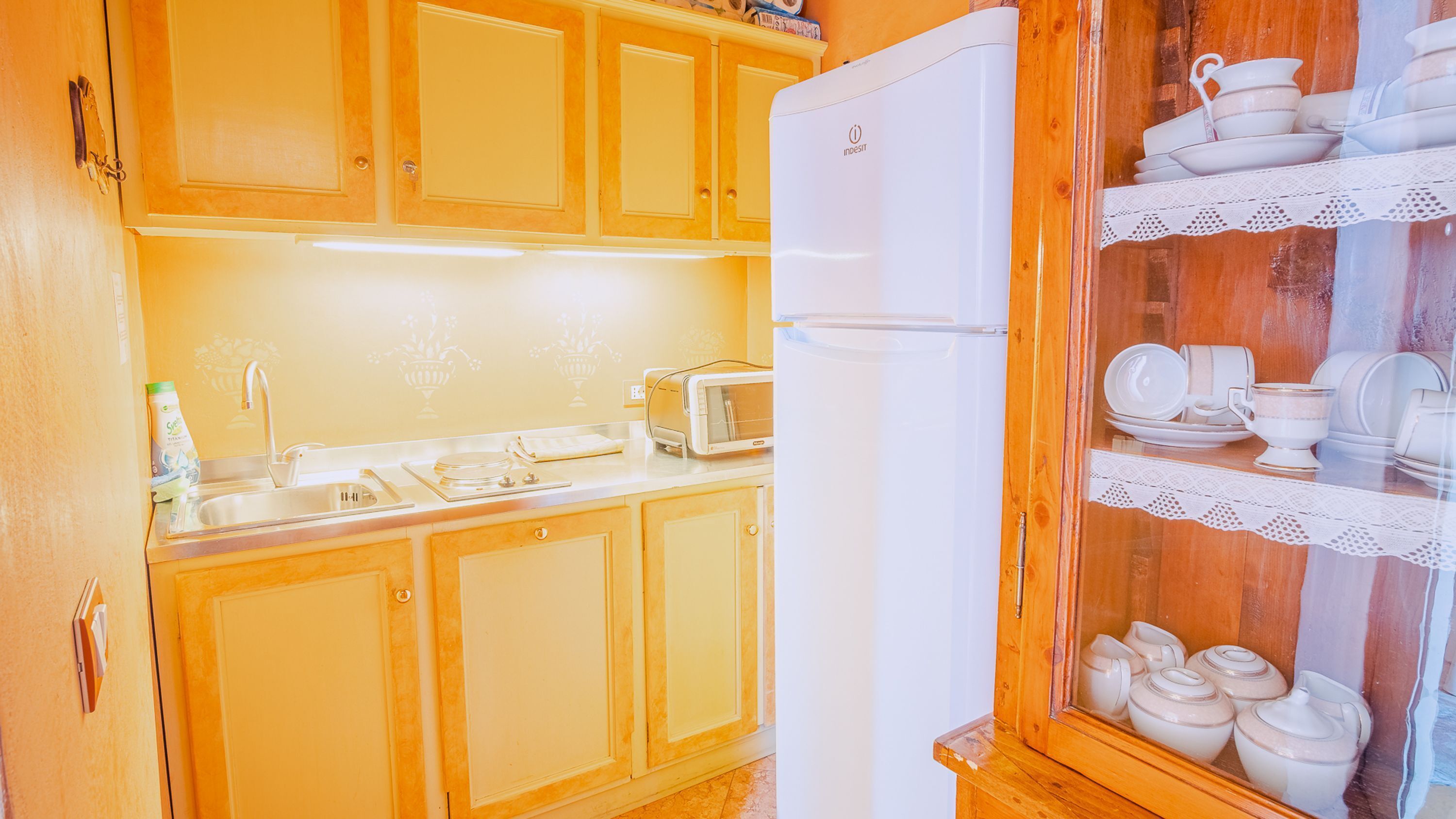 Eine Küche mit Holzausstattung, einem weißen Kühlschrank, einer Spüle, einem Toaster und einer Glastheke mit Geschirr.