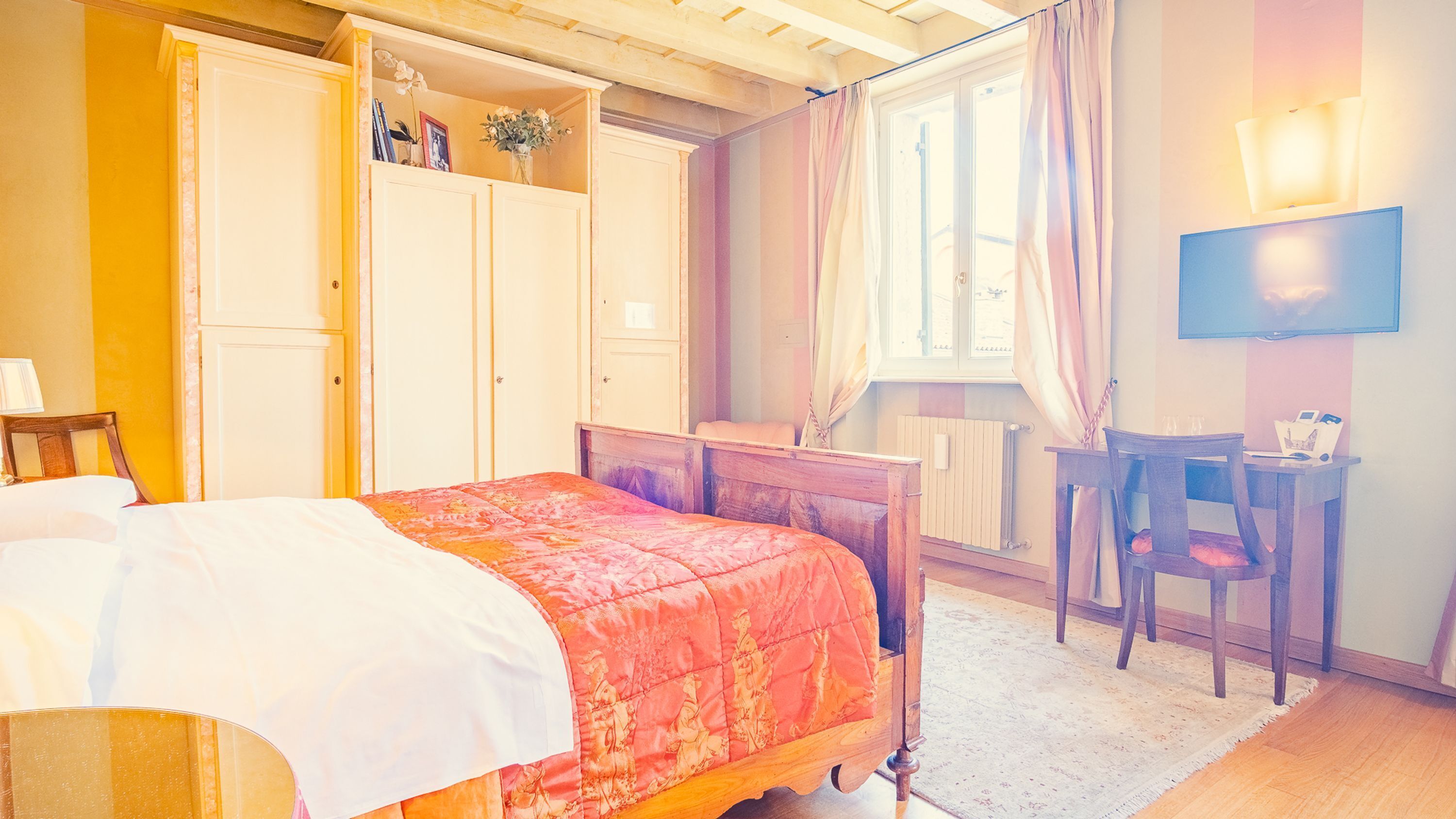 A bedroom with a bed, a desk, a chair, a wardrobe, and a television.