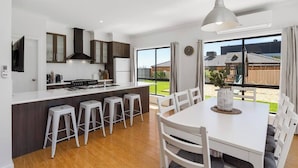 Een moderne keuken met een centraal eiland, witte barkrukken, en een eethoek met een witte tafel en stoelen.