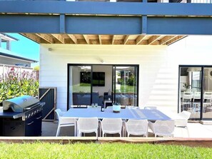 Une terrasse extérieure avec une table et des chaises, un barbecue et une porte-fenêtre coulissante donnant sur un espace abrité.