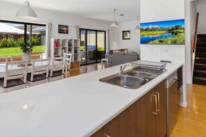 A modern kitchen with a large island, built-in dishwasher, and a dining area with white chairs.