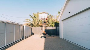 Un panier de basket dans un jardin, avec un garage et des palmiers.