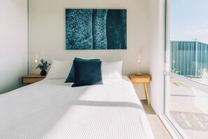 Et moderne hotelværelse med en stor seng, udsigt over byen og et vindue med udsigt til bygningen.