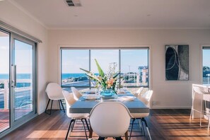 A dining area with a table set for two, large windows with a view of the sea, and a modern art piece on the wall.
