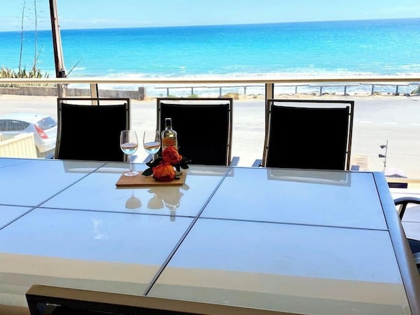 Ein Tisch mit zwei Stühlen, eine Spirituosenflasche und ein Glas Wasser auf einem Balkon mit Blick auf den Ozean.