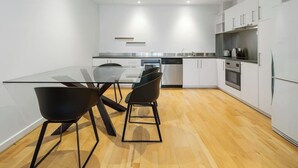 Een moderne keuken met witte kastjes, een glazen eettafel en zwarte stoelen.