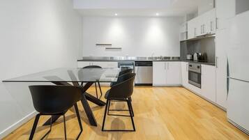 A modern kitchen with white cabinetry, a glass dining table, and black chairs.