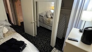 Une chambre d’hôtel avec un lit, une table de chevet avec une lampe, une armoire et une salle de bain visible à travers une porte ouverte.