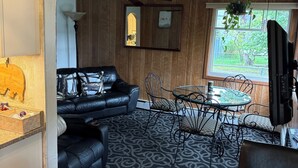 Un salon chaleureux avec un canapé en cuir noir, un tapis à motifs et un coin repas comprenant des chaises en métal et une table en verre.