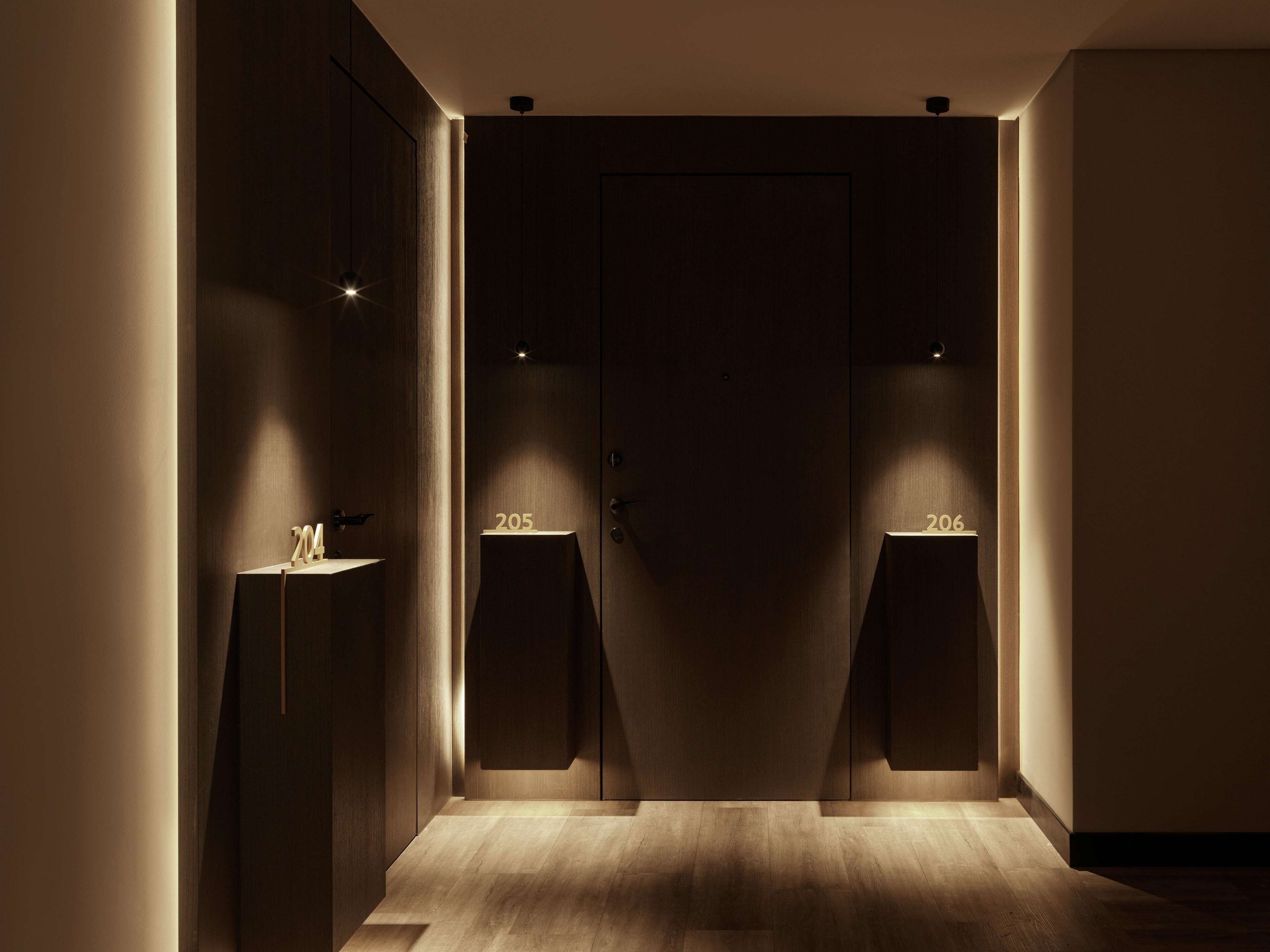 A hallway with a wooden floor and two illuminated numbers on pedestals, 205 and 206, indicating room numbers.